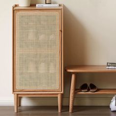 a wooden cabinet sitting next to a table with shoes on it and a vase in front of it