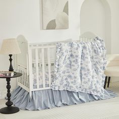 a white crib with blue and white bedding in a room next to a lamp