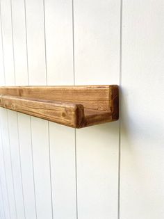 a wooden shelf mounted to the side of a white wall with wood planks on it