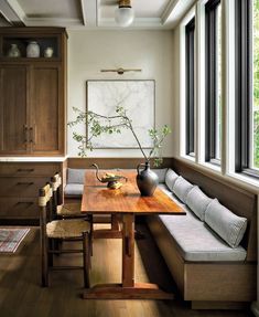 a wooden table sitting in front of a window next to a bench with pillows on it