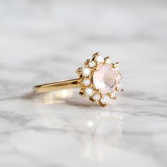 Sometimes when a girl says she likes to receive flowers as a gift, it's not the real flowers she means. Think twice and go for the safest thing - our Flora ring with Rose Quartz and Moissanites. Floral jewelry is where it's at! Perfect as a graduation gift, birthday gift, anniversary ring or promise ring. Details: Center stone Gemstone: Rose Quartz Stone Shape: Round Measurements: approx. 6mm Side stones Gemstone: Moissanite Shape: Round Measurements: 2mm (6), 1.5mm (6) Pictured in vermeil, avai Proposal Crystal Ring With Center Stone, Rose Gold Diamond Birthstone Ring For Proposal, Rose Cut Diamond Cluster Ring For Proposal, Rose Gold Crystal Ring For Proposal, Rose Cut Diamond Cluster Flower Ring As Gift, Cluster Flower Ring With Rose Cut Diamonds For Gift, Round Cluster Ring With Rose Cut Diamonds For Proposal, Proposal Cluster Ring With Rose Cut Diamonds, Wedding Flower Cluster Ring With Rose Cut Diamonds