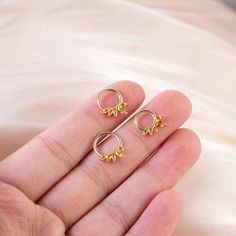 a hand holding two small gold earrings on it's fingers, one with leaves