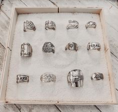 an assortment of rings in a box on a wooden table with white sand and wood planks