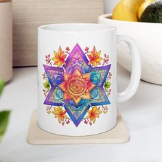 a white coffee mug with an intricate design on the front and side sitting on a coaster