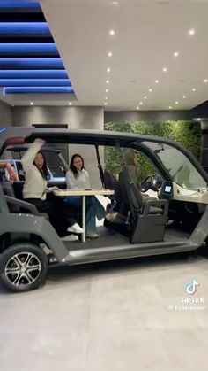 two women are sitting in the driver's seat of a golf cart that is on display