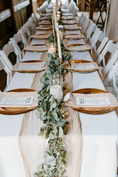 a long table set with place settings and greenery