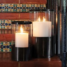 two lit candles sitting on top of a table next to a wall with colorful tiles