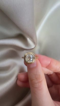 a person holding a ring with a diamond in it's middle, on top of a white cloth