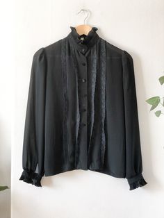 Vintage 60s black sheer secretary blouse. Features six button closures, button wrists, ruffle hem neck and sleeves, lace details up front and slightly puffed sleeves. A classic blouse for a classy someone.  Label: Style Rite Blouse Co. - Toronto Fits Like: women's small Color: black Fabrication: chiffon / polyester Condition: good vintage condition, normal signs of wear 14.5" shoulder 37" chest 35" waist 24" sleeve 24" length This item comes from a pet & smoke free building. For a look behind the scenes at our treasure hunting trips follow us at: + Instagram: @mostlymagicvintage + TikTok: @mostlymagik Retro Black Button-up Blouse, Formal Fall Blouse With Ruffled Collar, Formal Peter Pan Collar Top For Fall, Formal Peter Pan Collar Blouse For Fall, Workwear Button-up Blouse With Lace Cuffs, Button-up Blouse With Lace Cuffs For Work, Formal Blouse With Peter Pan Collar For Fall, Formal Black Tops With Lace Cuffs, Workwear Blouse With Lace Cuffs And Button-up