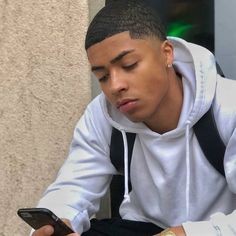 a young man sitting down looking at his cell phone while wearing a white hoodie