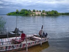 a boat sitting on top of a lake next to a shore covered in grass and trees