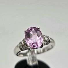 Indulge in the timeless allure of this vintage estate ring, crafted in luxurious 18k white gold. The focal point is a resplendent oval-cut kunzite, boasting a substantial 2.08 carats. Kunzite, known for its positive properties, brings a gentle, soothing energy and is often associated with matters of the heart. The captivating pink hue of the genuine kunzite is cradled in an elegant 4-prong setting, exuding a soft and romantic charm. Adorning the shoulders of the ring are genuine natural diamonds Oval Platinum Gemstone With Center Stone, Classic Oval Platinum Gemstones, Classic Oval Diamond Gemstones, Elegant Baguette Cut Topaz Ring With Accent Stones, Timeless Sapphire Ring With Accent Stones For Formal Occasions, Elegant Topaz Ring With Center Stone, Classic Diamond Gemstone With Center Stone, Elegant Oval Brilliant Cut Gemstones, Classic Oval White Gold Gemstones