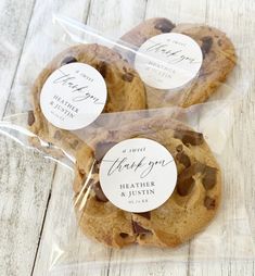 three chocolate chip cookies wrapped in plastic on top of a wooden table with thank you stickers