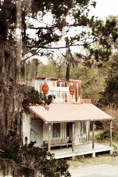 an old white house sitting in the middle of a forest with trees around it and a red roof