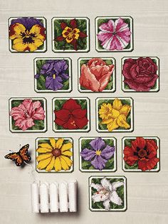 cross stitch flowers are arranged in squares on a white tablecloth with a butterfly nearby