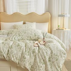 a bed with white and green comforters in a bedroom next to a lamp on a table