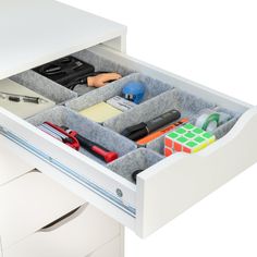 an open drawer with various office supplies in it on top of a white desk and drawers