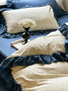 a bed with blue sheets and white flowers in a vase on the end table next to it