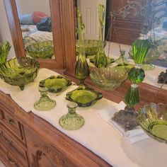 green glass dishes and vases sit on a counter in front of a large mirror