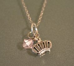 a silver necklace with a crown charm and a pink crystal bead hanging from it