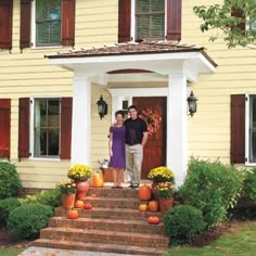 a man and woman standing in front of a house with pumpkins on the steps