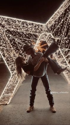 a woman carrying a child in her arms with christmas lights on the wall behind her