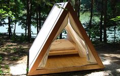 a tent set up in the woods with a bed on it's side and trees around