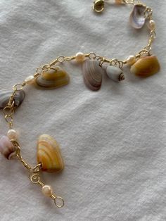 The handcrafted Mira bracelet features freshwater pearls and hand-collected coquina clam shells and spiral sea shells from the California coast line. * Shells are a stunning array of sunrise purple, orange, and white. Pearls are lovely soft cream. Gold copper wire is tarnish resistant.  * This bracelet measures 8 inches but can lengthened or shortened upon request and features a lobster clasp closure.  * *Please note that shells are natural and unaltered, and may be delicate. All shells are genuine and ethically sourced. Although material is tarnish resistant, please follow instructions on care card to maintain the integrity of this product.* Shell Bracelet Aesthetic, Shell Jewelry Ideas, Sunrise Purple, Sea Shell Bracelet, Freetime Activities, No Ordinary Girl, Clam Shells, Coast Line