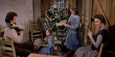 three women and two children sitting around a christmas tree in a room with wooden walls