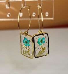 Clear resin with paper flower inside. Gold Flower Resin Earrings, Resin Flower Charm Drop Earrings, Resin Drop Earrings With Flower Charm, Handmade Resin Flower Shaped Earrings, Handmade Resin Flower-shaped Earrings, Flower-shaped Floral Print Earrings For Gift, Floral Print Flower Earrings For Gift, Resin Earrings With Flower Charm, Resin Flower Earrings With Flower Charm