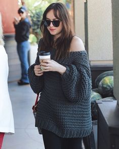 a woman holding a coffee cup and looking at her cell phone while walking down the street