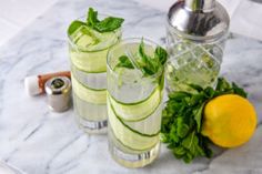 three glasses filled with cucumber, mint and lemonade on a marble table