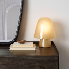 a table lamp sitting on top of a wooden dresser next to a mirror and books