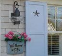 a blue shuttered window with flowers and a welcome sign on the side of it