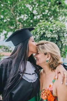 two women in graduation gowns are kissing each other and smiling at the same time