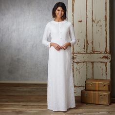 a woman wearing a white dress standing in front of an old door and suitcases