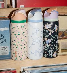 three water bottles sitting on top of a wooden shelf next to books and cdshelves