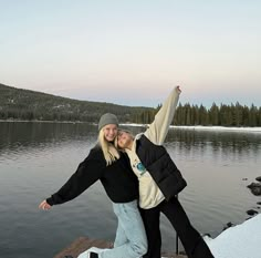 two women are posing for a picture on the dock by the water with their arms in the air