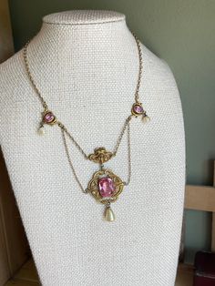 A great example of Art Nouveau jewelry 1880-1915. Gold Filled.  This choker features an Art Nouveau design with pink faceted glass and glass coated pearls.  The central drop has a large cushion shaped faceted pink glass bezel set.  Above is a goddess with flowing hair.  The drop measures 2.25" from top to bottom.  There are decorative pink glass set links with glass coated pearls.  Barrel clasp in working order. The piece overall is in very good.  Please note some loss to the coating on the round pearls.  The length is 14.25".  These pieces were meant to be worn tight to the neckline.  Possible to add some extra chain at the back to enlarge.  The color of the faceted glass is a beautiful pink -mimics a pink sapphire.  Rarely do I get such a fine example in hand.  14 day return policy. Formal Pink Cabochon Necklace, Vintage Pink Gemstone Jewelry, Vintage Pink Gemstone Necklace, Vintage Pink Oval Necklace, Elegant Pink Cabochon Necklace, Victorian Jeweled Jewelry From Vintage Collection, Antique Pink Jewelry For Formal Occasions, Pink Oval Victorian Jewelry, Art Deco Pink Jewelry For Wedding