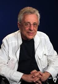 an older man sitting in a chair with his hands folded