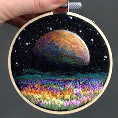 a hand is holding up a small embroidered ornament with an image of a planet in the sky