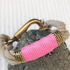 a pink and gold bracelet sitting on top of a rock next to a metal hook