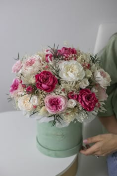 a woman holding a bouquet of flowers on top of a white table next to a green bucket