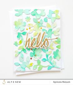 a card with the word hello written in gold foil on it and green leaves surrounding it