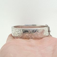 A vintage sterling silver snap bangle bracelet with engraved patterns on the front and a smooth plain back, also fitted with a safety chain. The bracelet is fully hallmarked with date letter "0" dating back to 1963. It opens and closes as it should. It measures internally from clasp too hinge approx. 5.74 cm so your wrist needs to be slimmer than this to fit when it is closed, it is approx. 16 mm wide and it weighs approx. 28 g. Condition is good true vintage. Please check out the other items in Heirloom Silver Engraved Bracelets, Ceremonial Engraved Sterling Silver Bracelet, Classic Silver Engraved Bangle, Victorian Sterling Silver Engraved Wedding Bracelet, Ornate Engraved Sterling Silver Bracelet, Vintage Silver Cuff Bracelet With Engraving, Silver Vintage Engraved Cuff Bracelet, Vintage White Gold Bracelets Stamped 925, Vintage Silver Engraved Cuff Bracelet