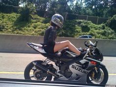 a woman sitting on top of a motorcycle in front of a road with trees and bushes behind her