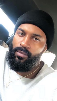 a man with a beard wearing a beanie and looking at the camera while sitting in a car