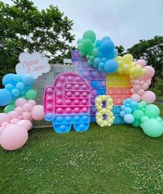 a bunch of balloons that are sitting in the grass near a sign and some trees