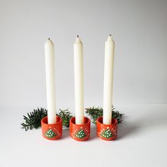 three white candles are sitting in red cups