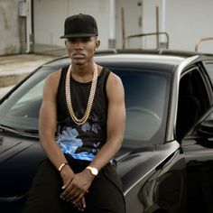 a man sitting on top of a car next to a black car and wearing a hat